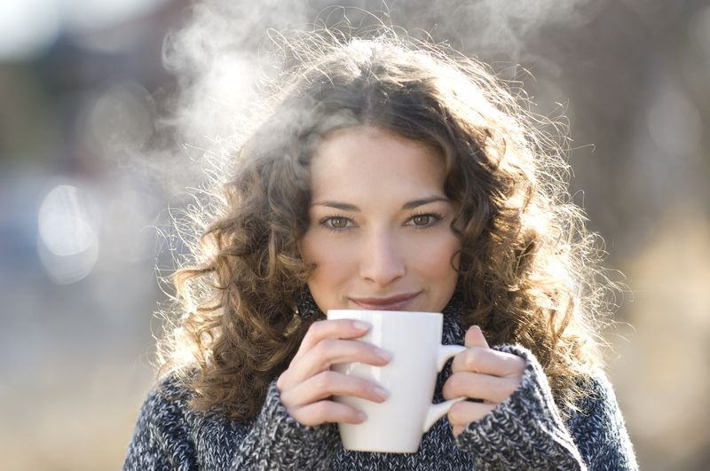 熱いお茶を飲むプルオーバーのブルネットの女性